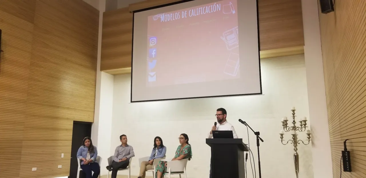 Andrés Londoño en el atril de un panel, con cuatro panelistas sentados y la presentación "Modelos de calificación"