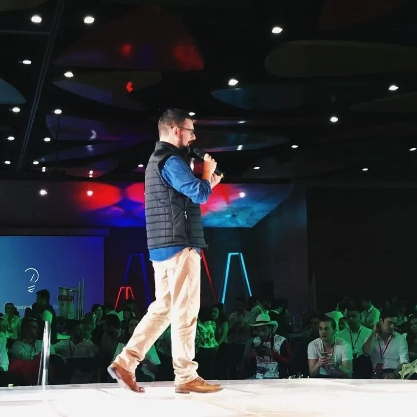 Andrés Londoño con micrófono en el escenario de StartCo Medellín, frente a un auditorio lleno